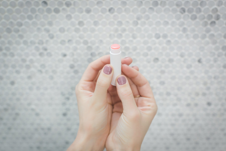 Hands holding a white lip balm stick over a tiled background