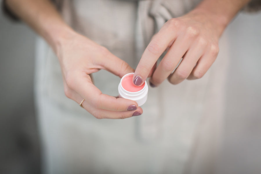 Hand dipping a finger into a pink lip balm jar